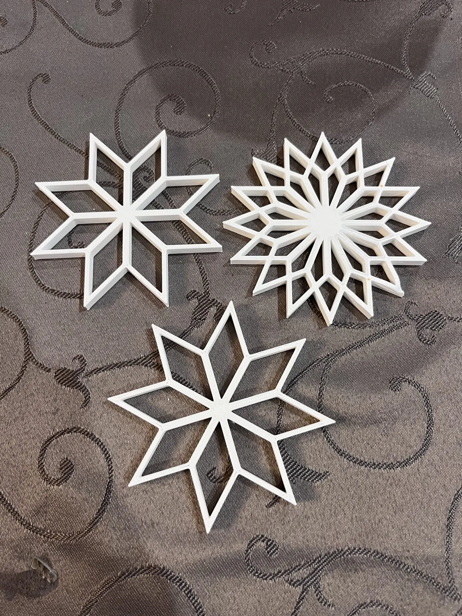 Trois étoiles décoratives blanches ajourées, imprimées en 3D, posées sur une nappe grise