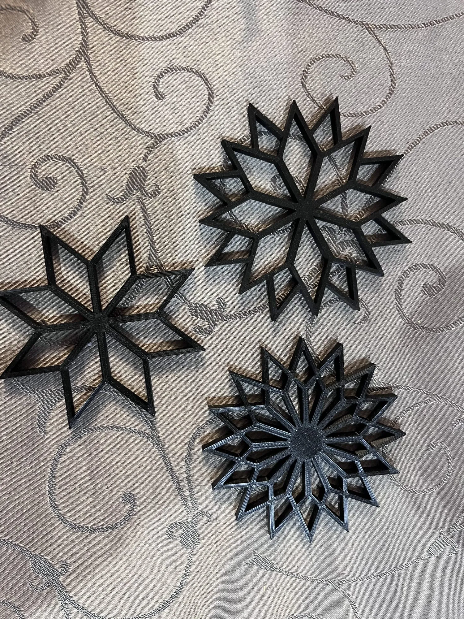 Trois étoiles décoratives noires ajourées, imprimées en 3D, posées sur une nappe grise