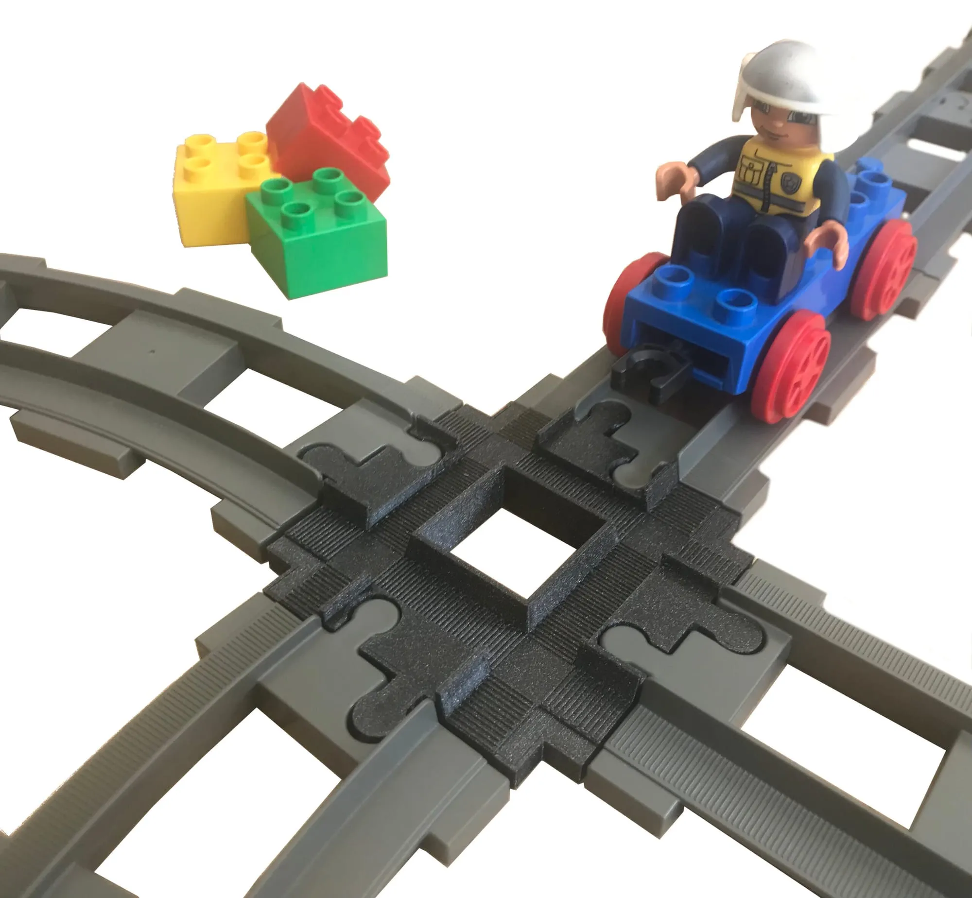 Croisement 4 voies noir au centre de rails DUPLO, un petit train DUPLO bleu avec son conducteur s’y engage