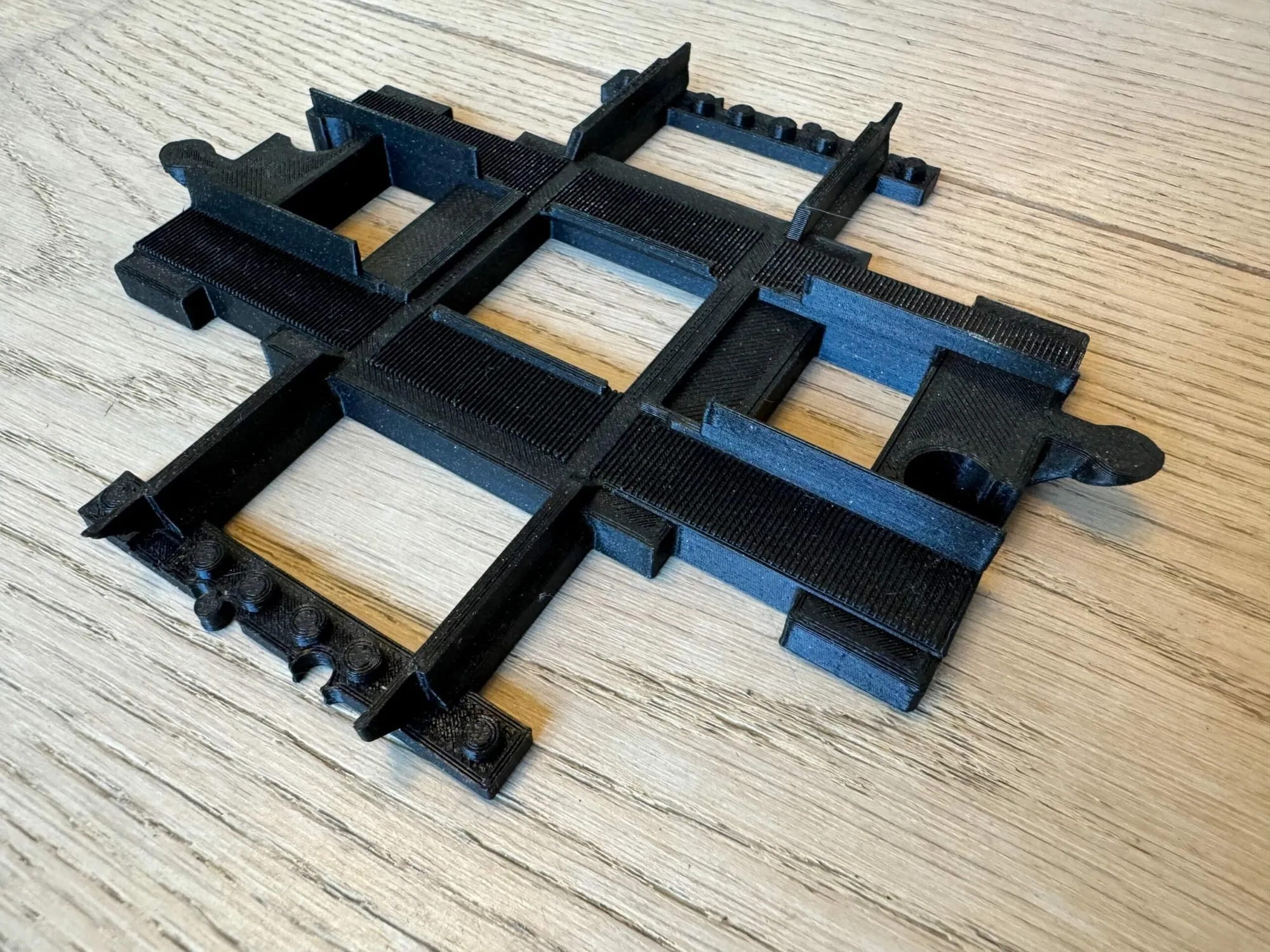 Croisement 4 voies noir imprimé en 3D, posé sur un parquet
