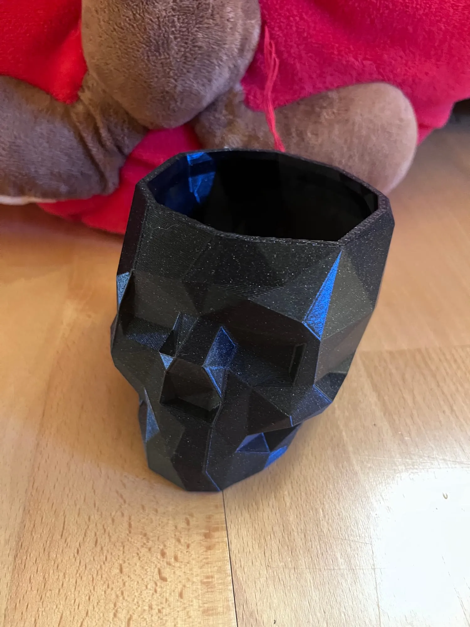 Pot en forme de crâne low poly noir, vu de face, posé sur une table en bois