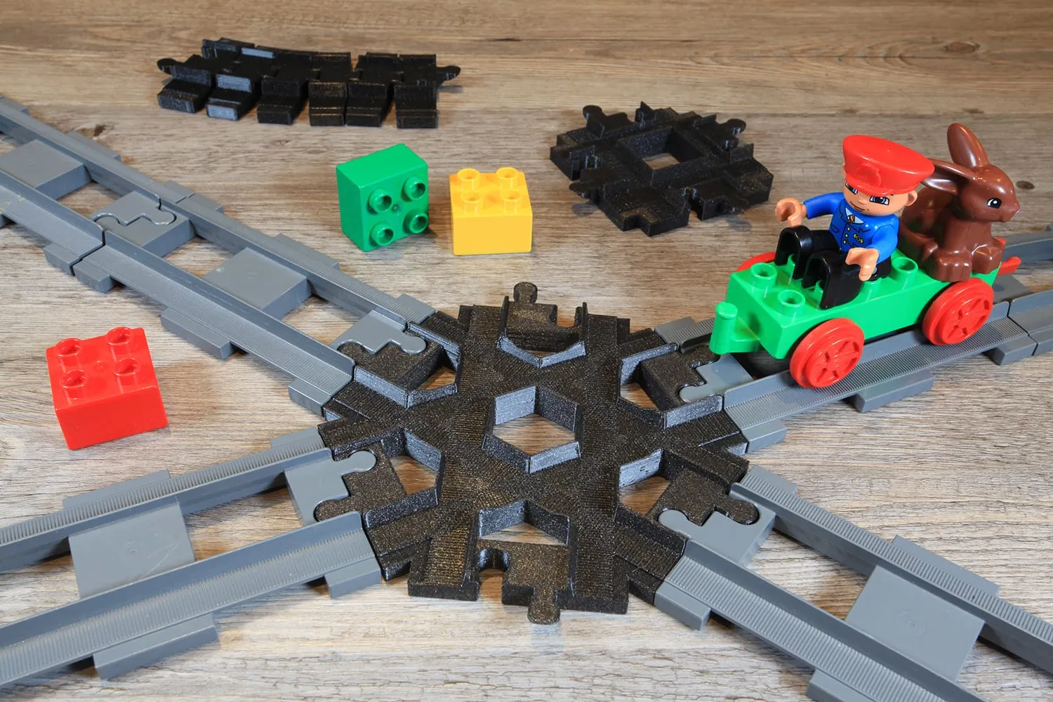 Croisement 6 voies noir posé sur des rails DUPLO croisés, avec un train DUPLO vert et des briques colorées