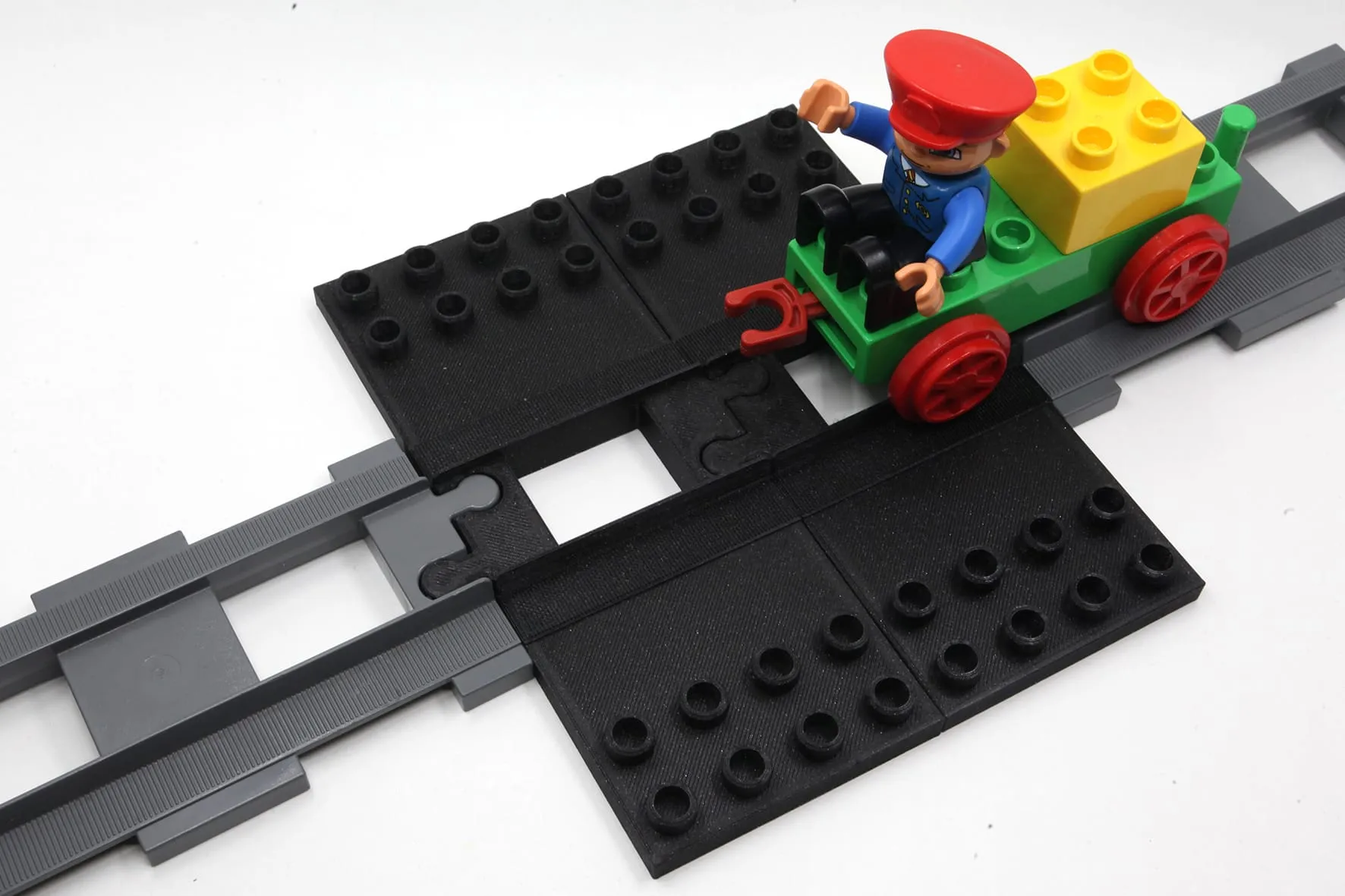 Plaque noire à plots posée à plat sur un rail DUPLO, un petit train DUPLO avec son conducteur s’y engage