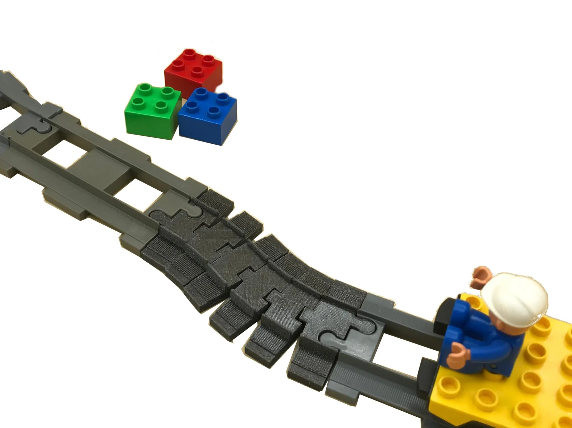 Rail flexible noir qui se courbe entre des rails DUPLO, avec un petit train DUPLO jaune et des briques colorées