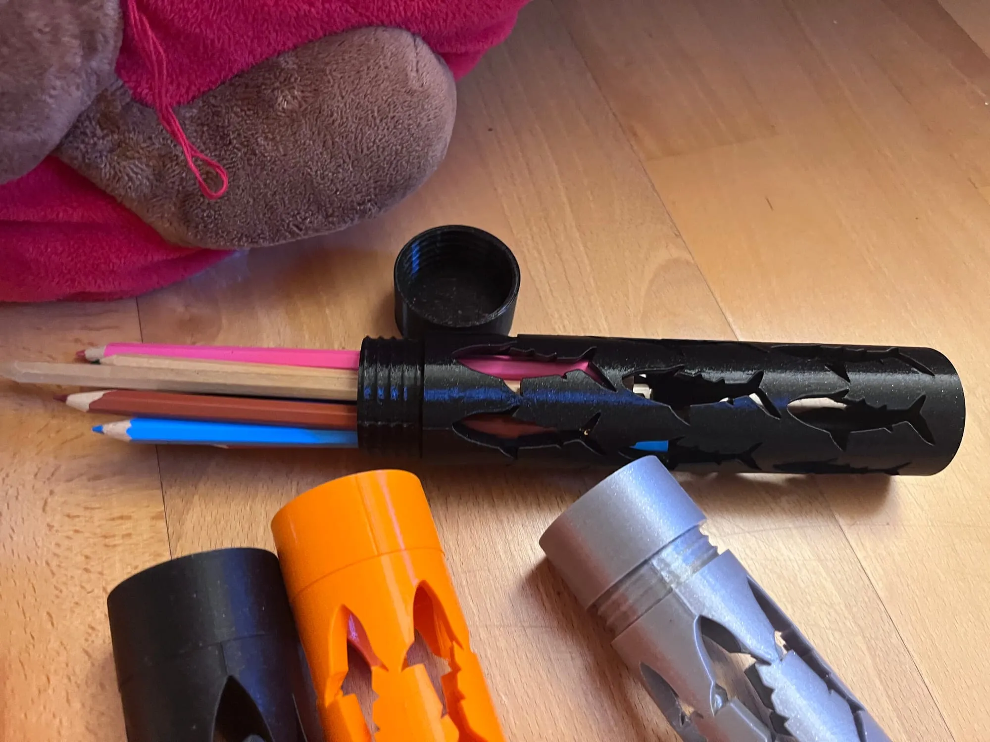 Étui noir ouvert d’où sortent des crayons de couleur, entouré d’étuis orange, noir et gris