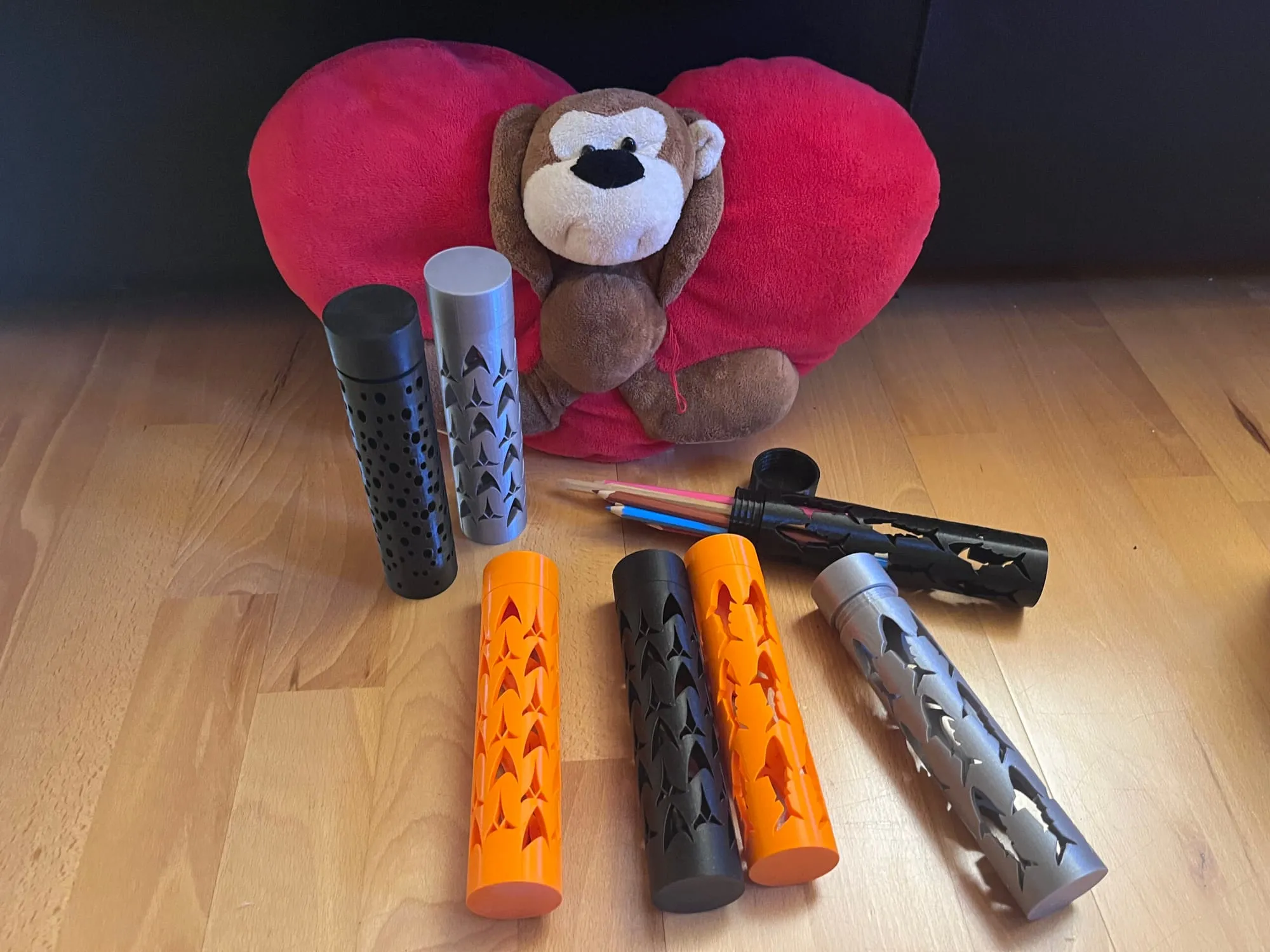 Série d’étuis cylindriques noirs, gris et orange alignés devant une peluche singe