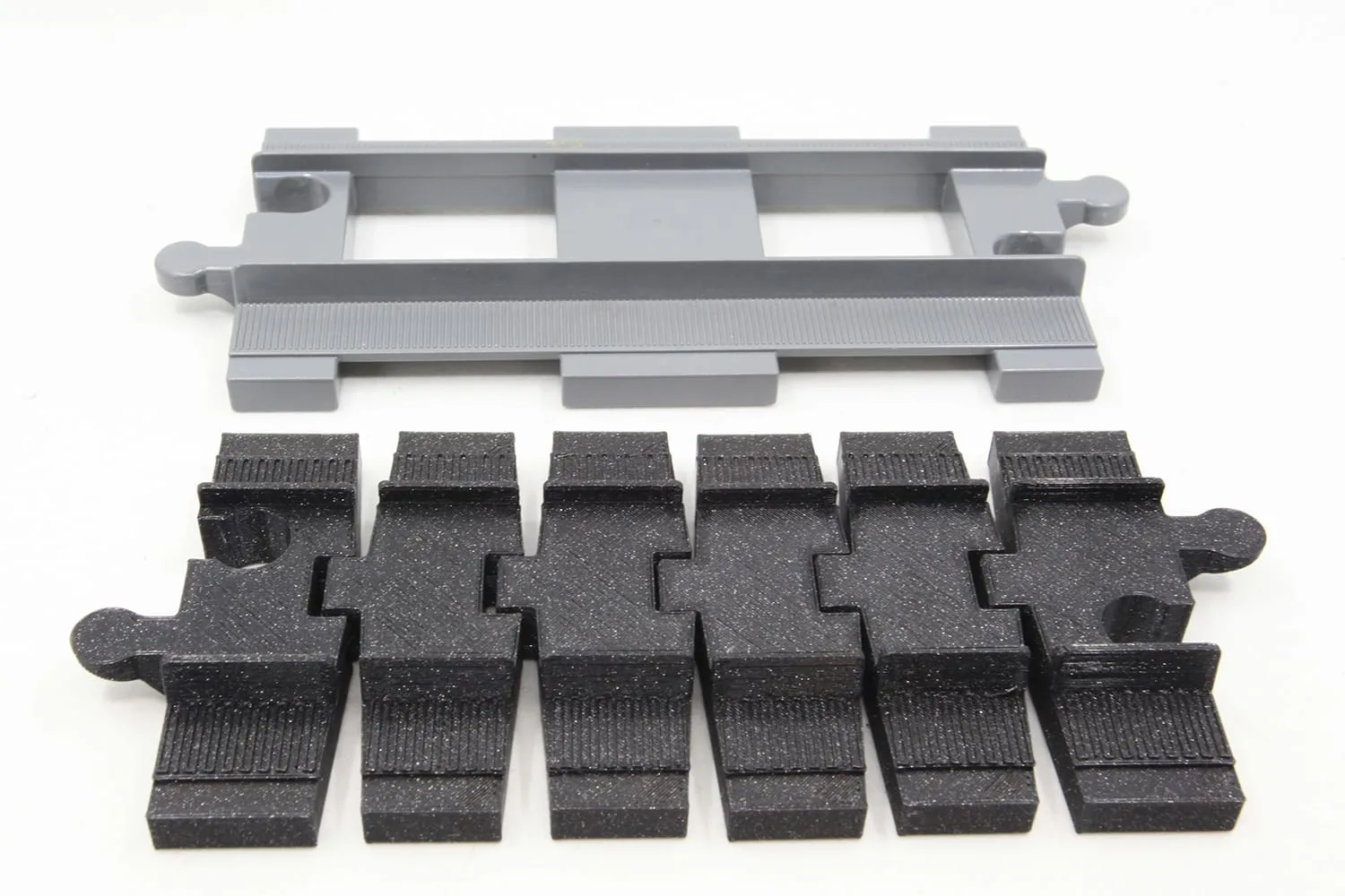 Rail DUPLO gris clair posé au-dessus d’un rail flexible noir, pour comparer les longueurs
