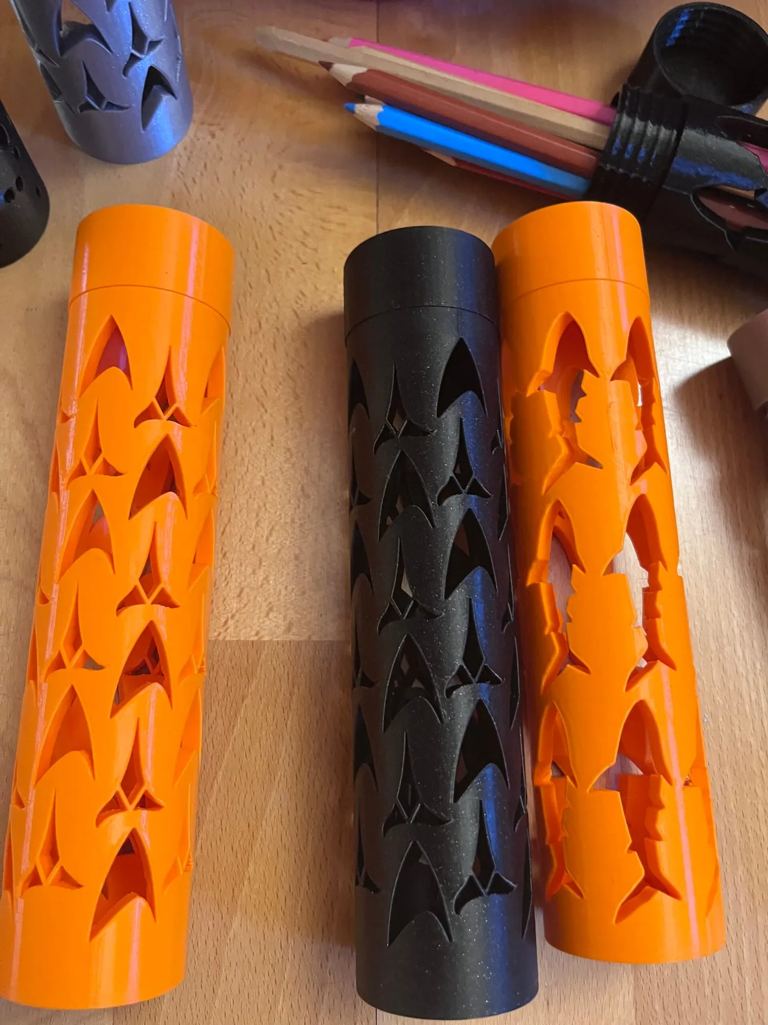 Étuis cylindriques ajourés orange et noir, vus de dessus