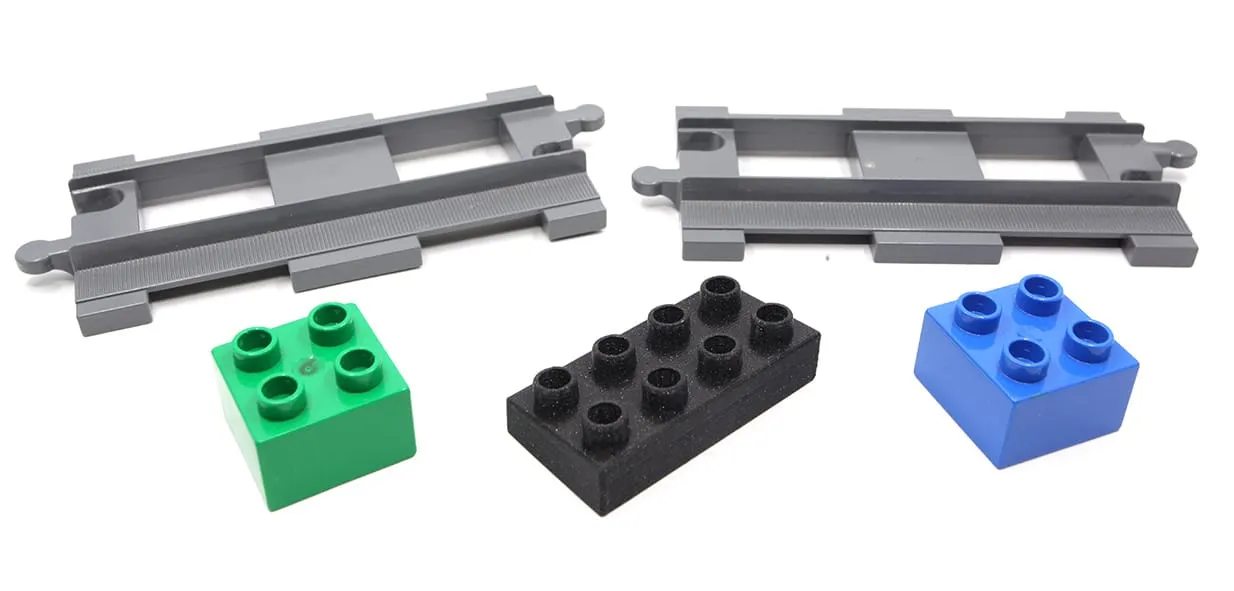 Deux rails de train DUPLO, deux briques DUPLO verte et bleue et une brique noire imprimée en 3D