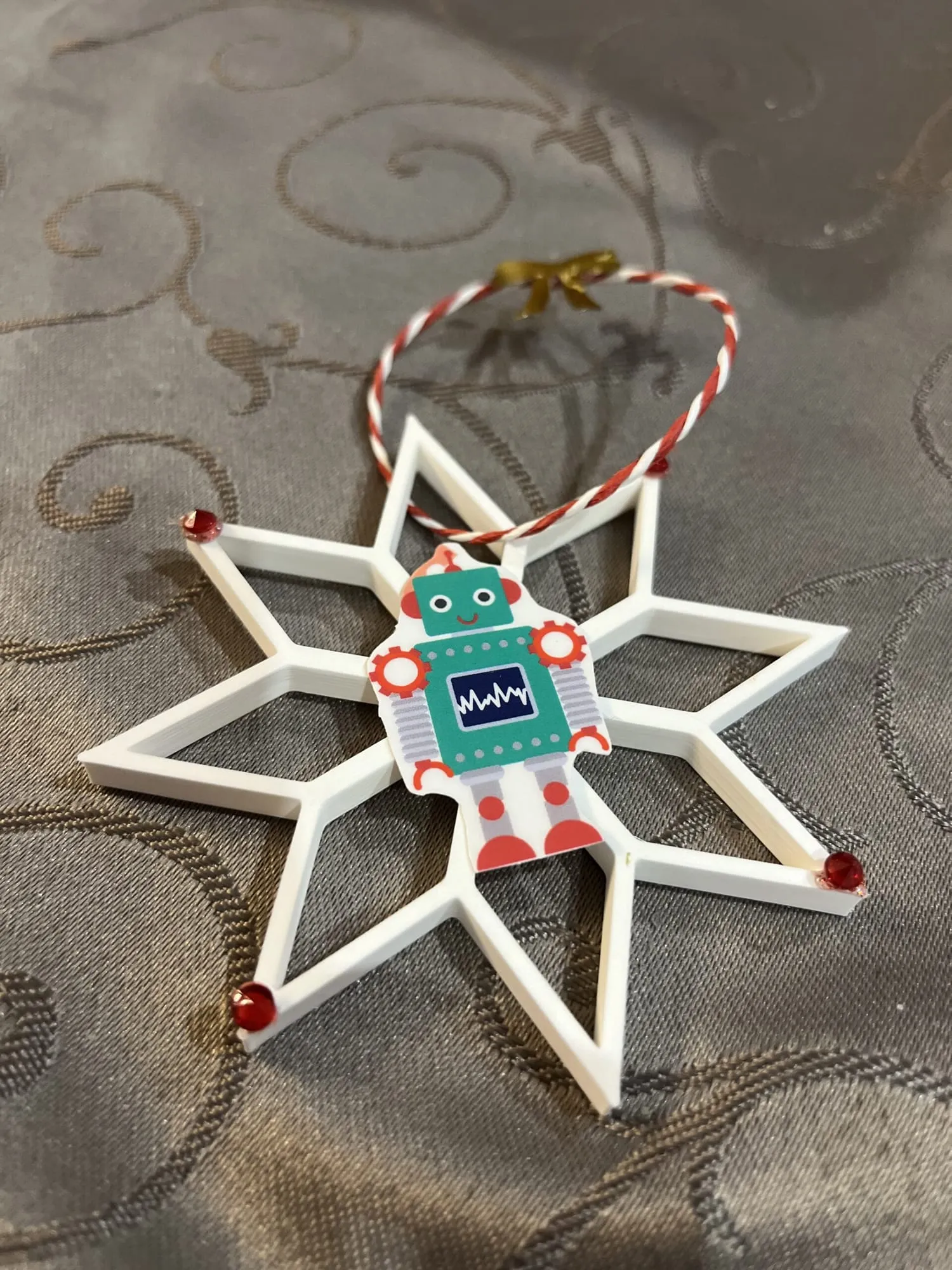 Étoile blanche décorée d’un petit robot en papier et d’une cordelette rouge et blanche, à suspendre