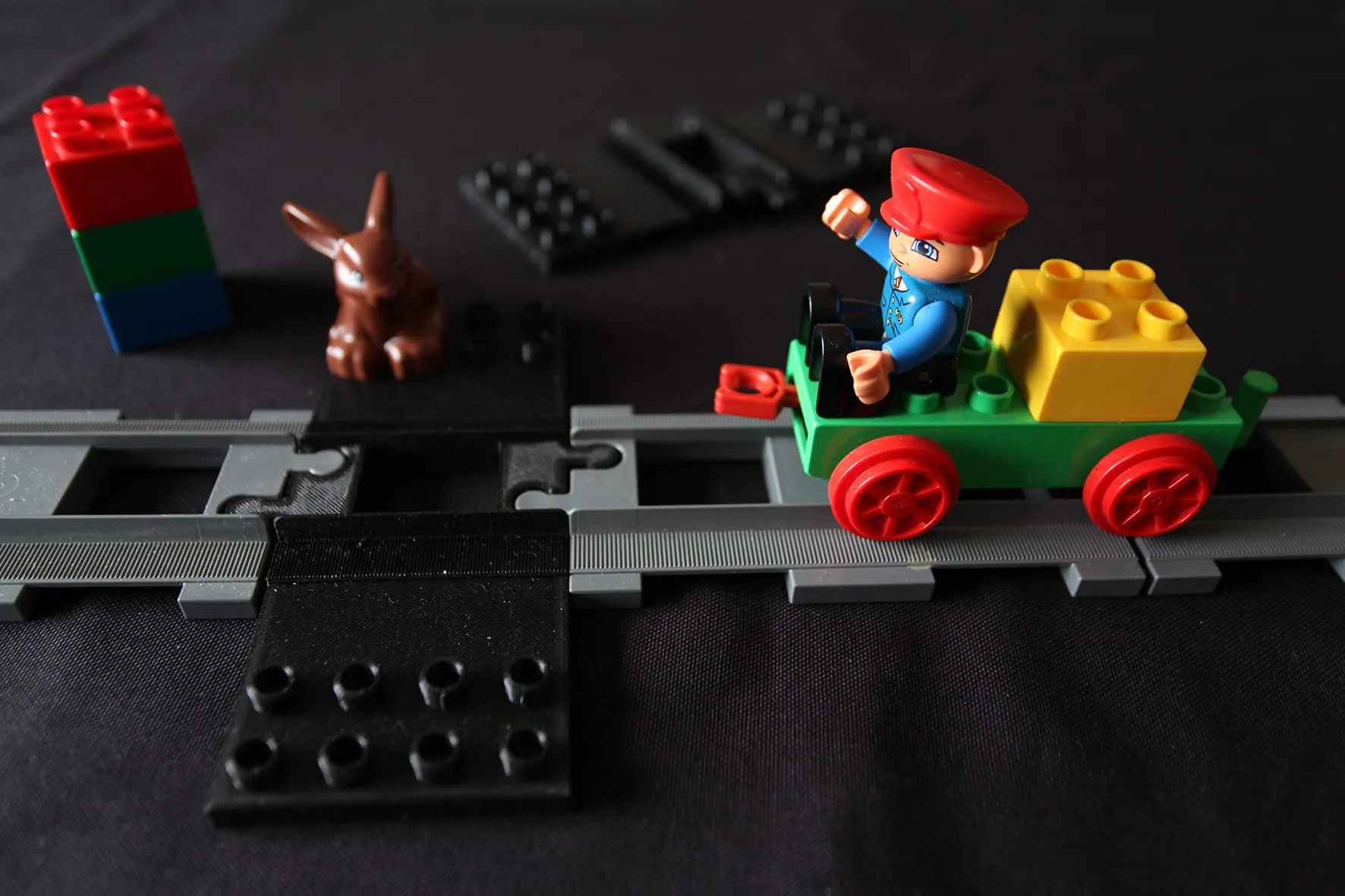 Train DUPLO vert traversant la plaque noire posée entre les rails, près d’un lapin et d’une tour de briques