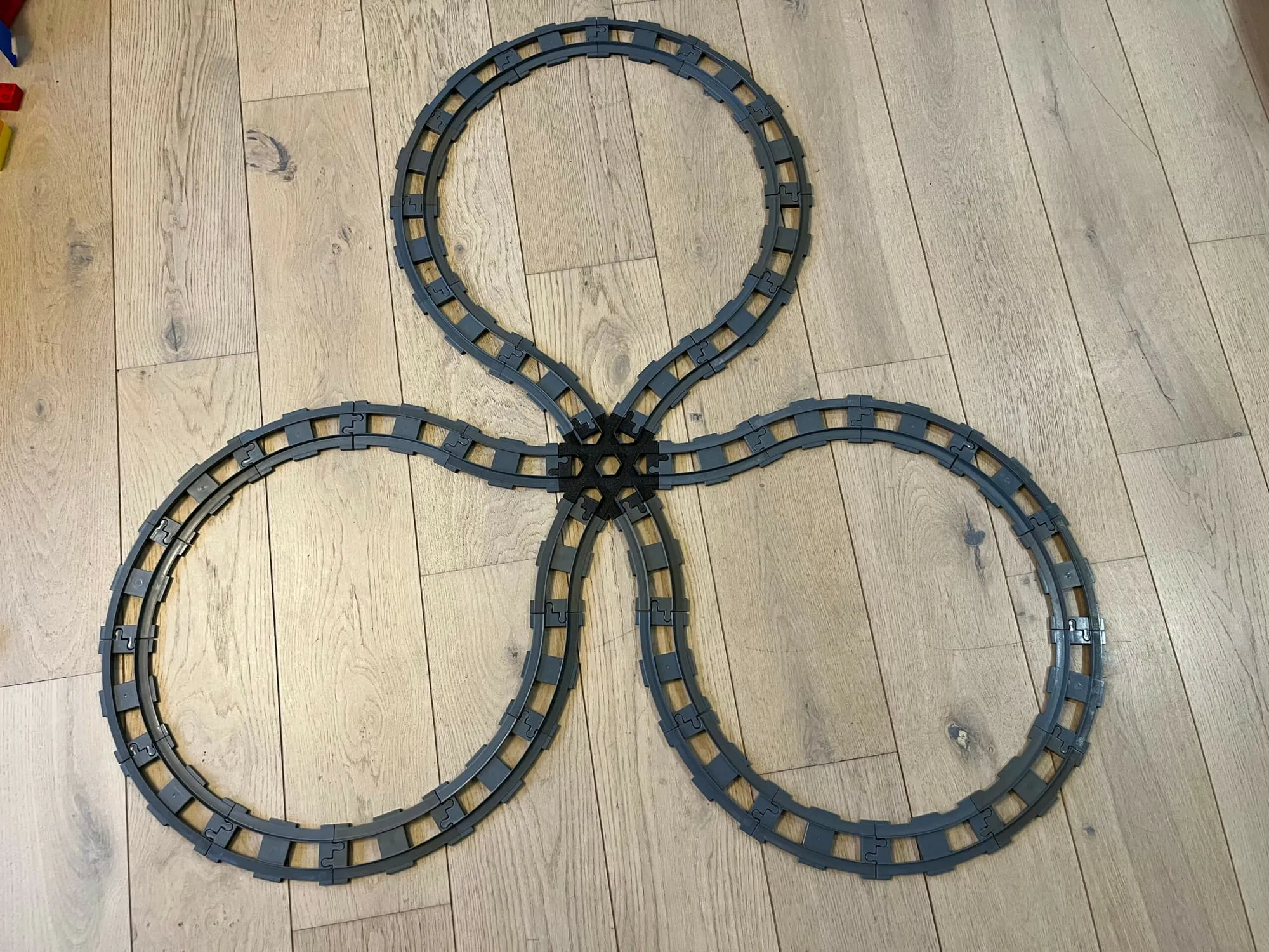 Circuit DUPLO en trèfle à trois boucles autour du croisement 6 voies noir, posé sur un parquet