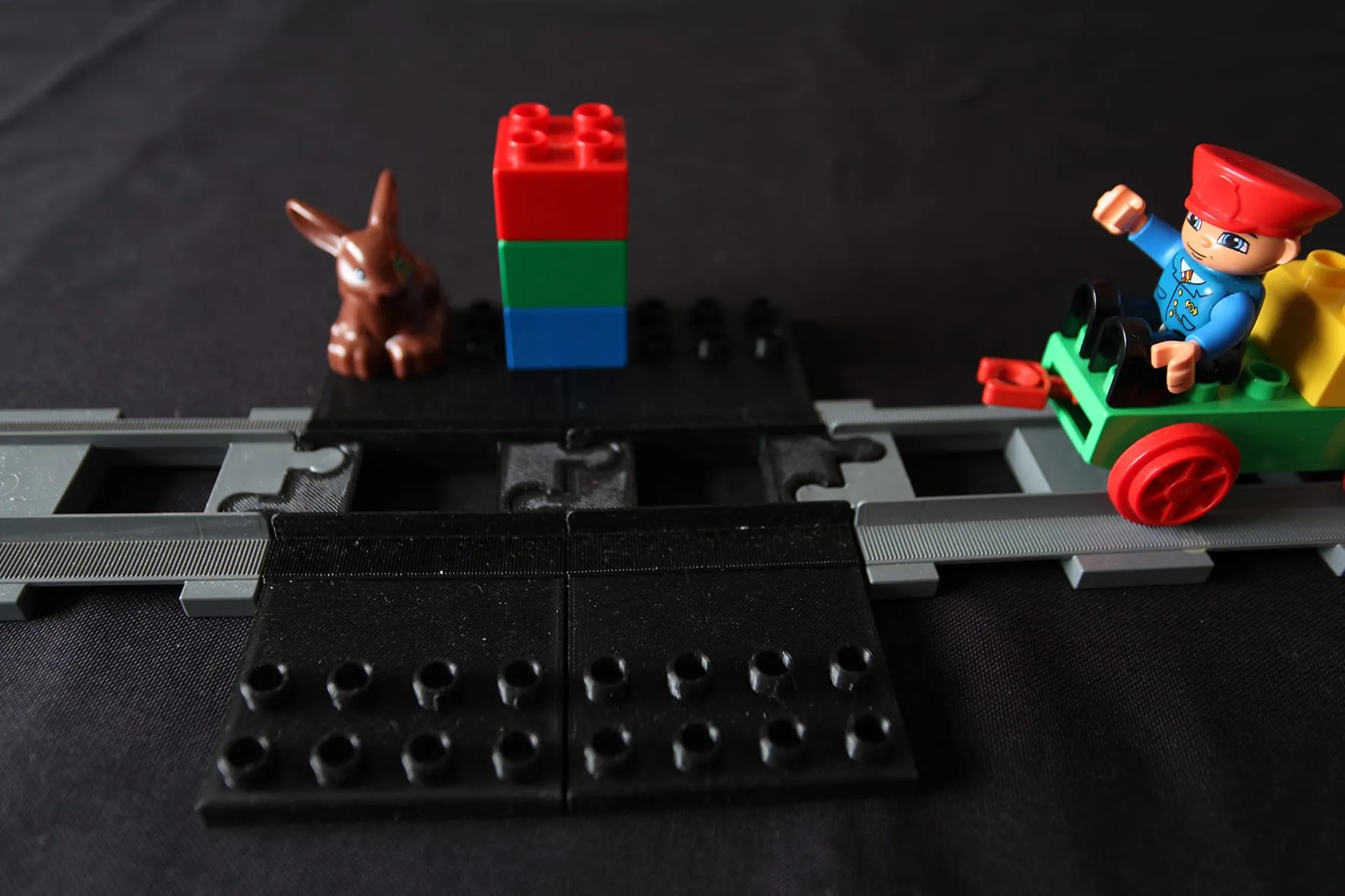 Plaque noire sur les rails DUPLO, un train vert à droite et un lapin à gauche