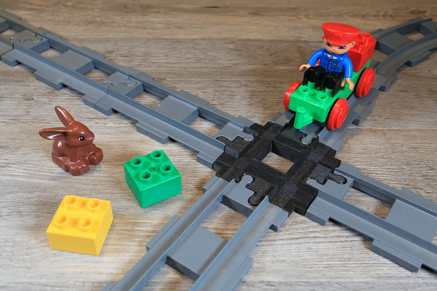 Train DUPLO vert avec son conducteur traversant le croisement noir, à côté d’un lapin et de briques DUPLO